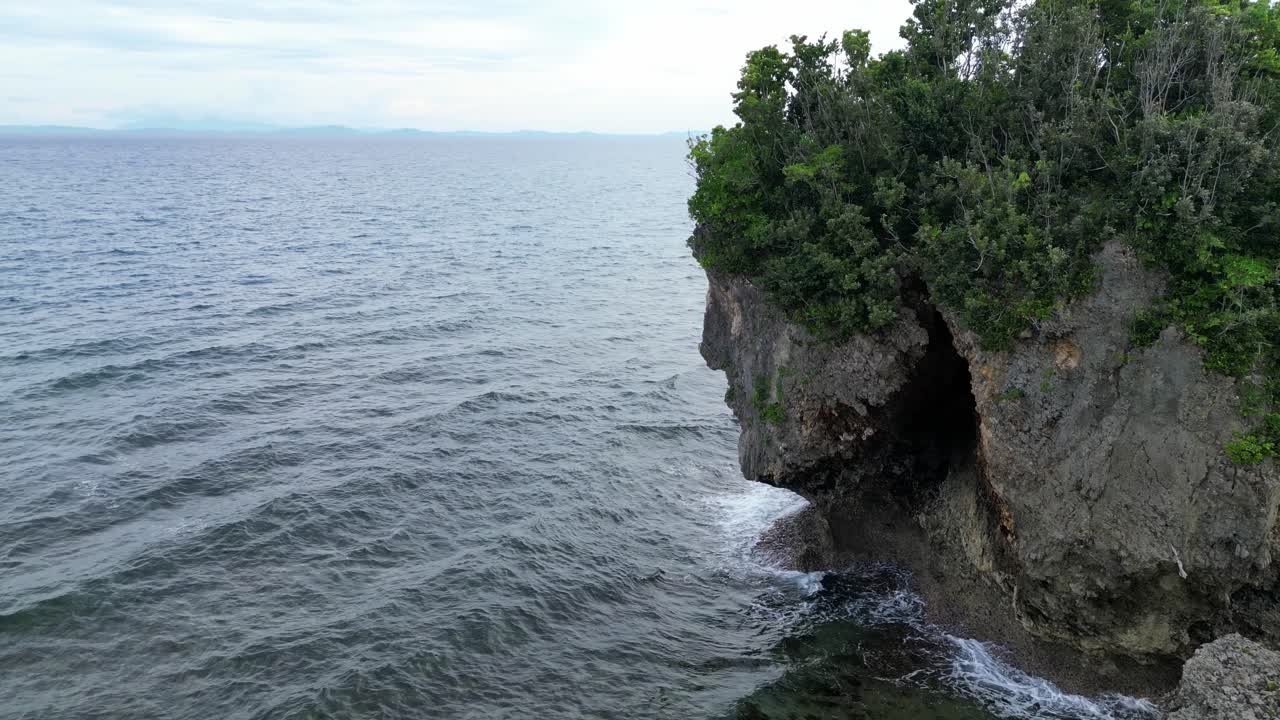tiro aéreo aproximado de uma rocha maciça no oceano, ondas batendo nela, revelando uma paisagem de nuvens de tirar o fôlego e uma ampla baía em catanduanes, filipinas