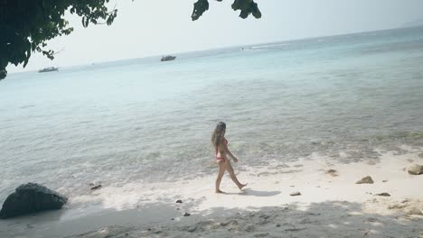 Una-Chica-Con-Traje-De-Baño-Brillante-Camina-Por-La-Playa-Del-Océano-Contra-El-Cielo