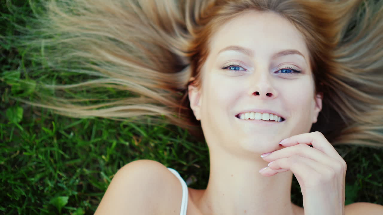 Una donna attraente giace sull'erba verde. I suoi capelli sono splendidamente distesi intorno.