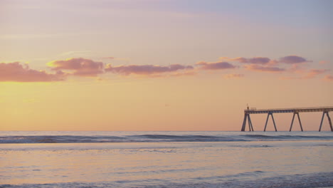 una espectacular puesta de sol en la playa naranja con nubes claras y un embarcadero en la distancia