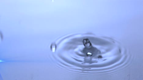 Animation-Von-Wassertropfen,-Die-Mit-Leuchtendem-Licht-In-Blaues-Wasser-Fallen