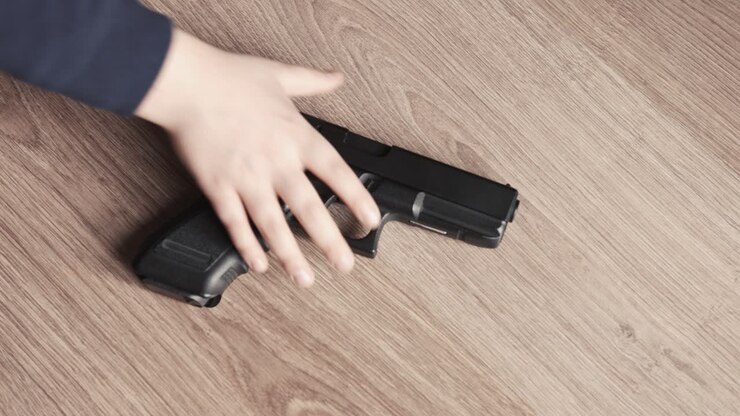 Adult offering a nine millimter gun to a young boy at home close up