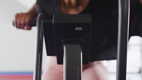 Video-close-up-of-determined-african-american-woman-on-exercise-bike-working-out-at-a-gym