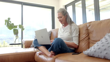 mujer caucásica sentada en el sofá, usando una computadora portátil