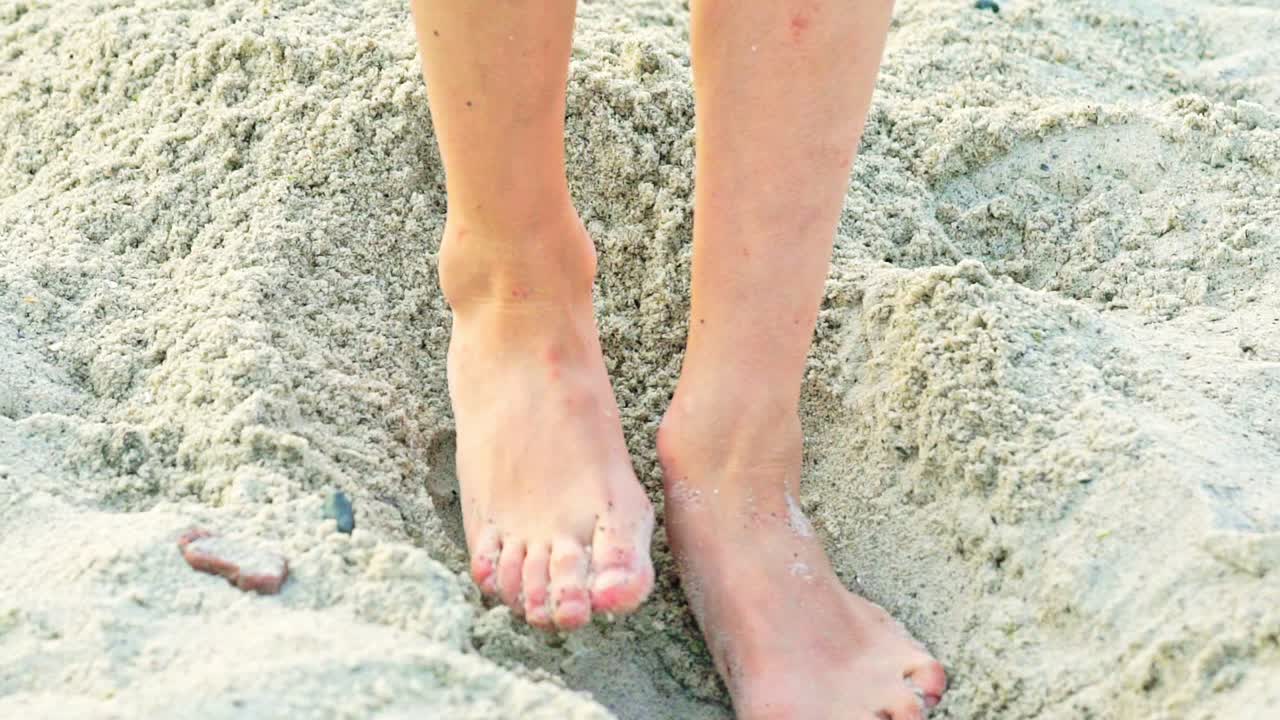 A kid gets up in a sandy pit with his legs to measure it and continues to expand its length and width. Close-up.