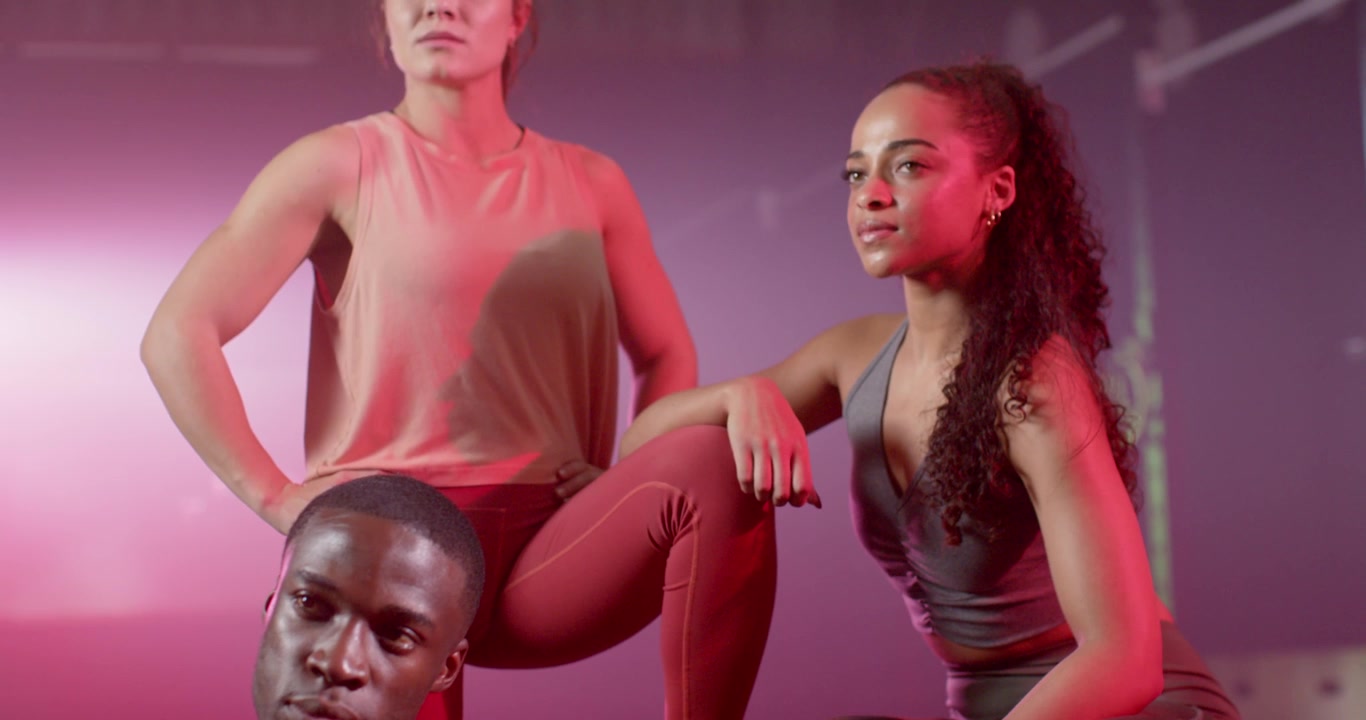 Diverse team in sportswear posing as camera panning under pink-purple lights, haze for shoot