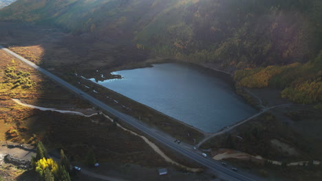 Aerial View of a Serene Lake Alongside a Road Winding Through Autumn Mountains