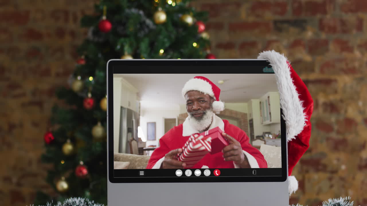 hombre afroamericano senior en disfraz de santa en videollamada en la computadora, con árbol de navidad