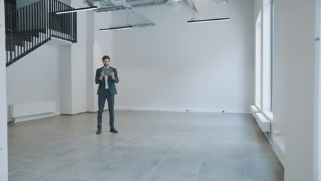 businessman standing in empty office and map it with an augmented reality software on a tablet computer. entrepreneur wears a suit. room has tracking points for video software.