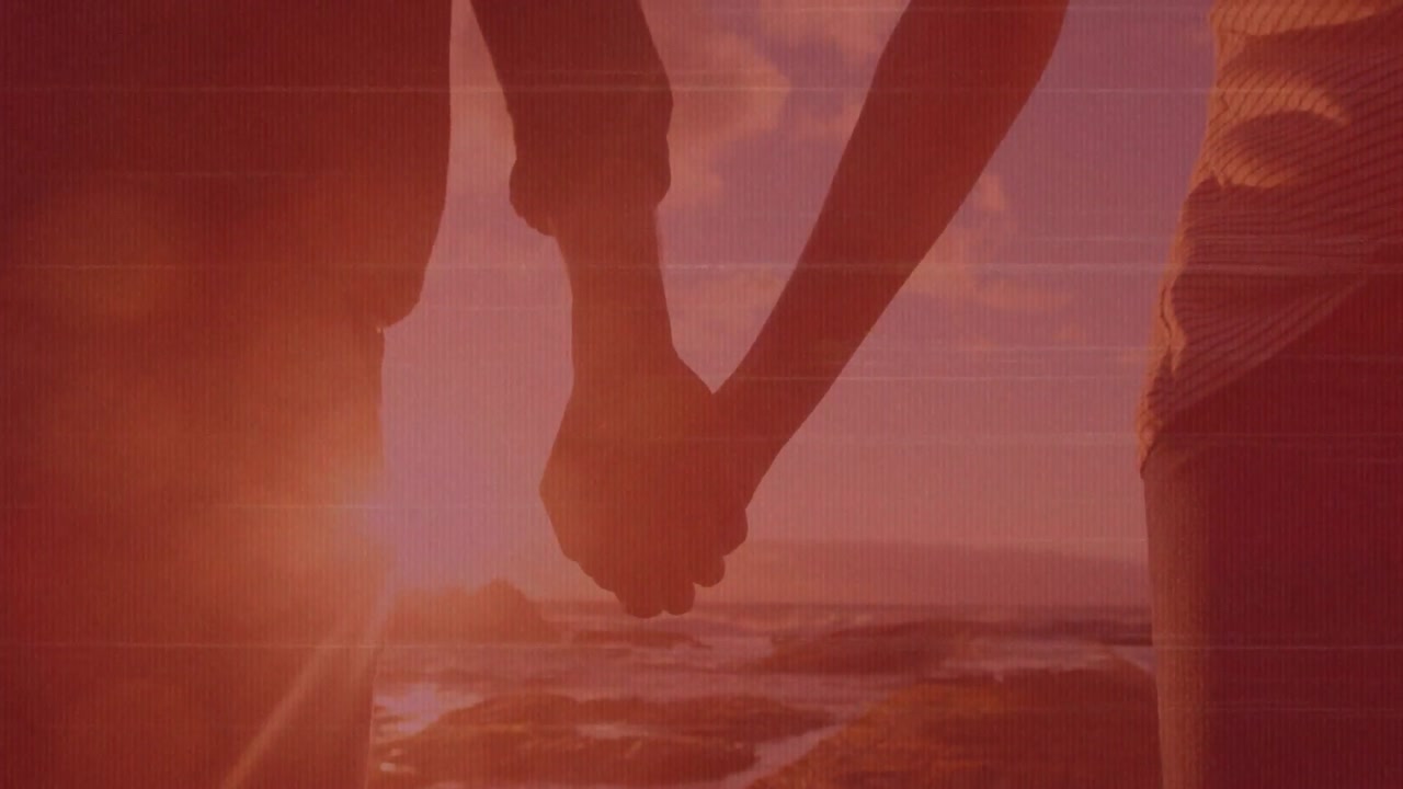 Couple arriving rocky shore and standing holding hands, camera closing on golden sunset for travel