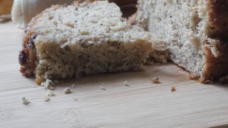 top view of sliced ​​banana bread and half cut banana bread on wooden board with a banana in the back. crumbs