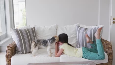 chica caucásica pasando el tiempo en casa, acostada en el sofá con máscara facial, jugando con su perro, en cámara lenta