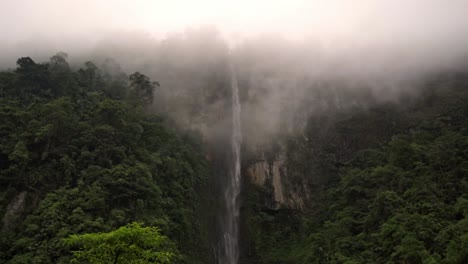 waterfall cascading down a high, rocky cliff face along the trail to quebrada gata. the surrounding lush, green rainforest is partially obscured by fog, creating a mystical and immersive atmosphere