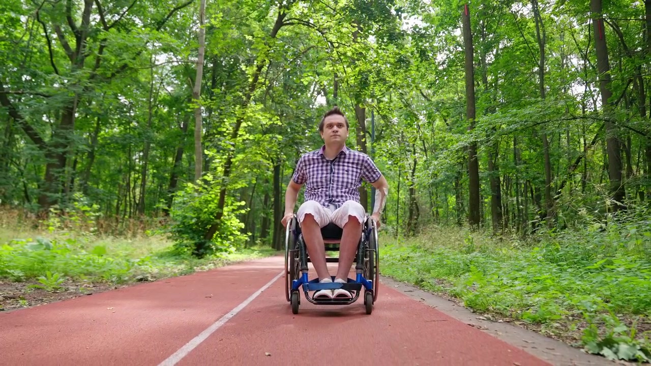 Young Man in Wheelchair Sitting on a Red Track in a Green Forest