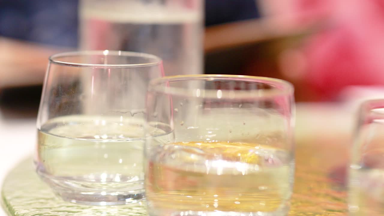 Close-up of glasses on a table with background motion. Soft lighting and shallow depth of field create a warm, intimate atmosphere