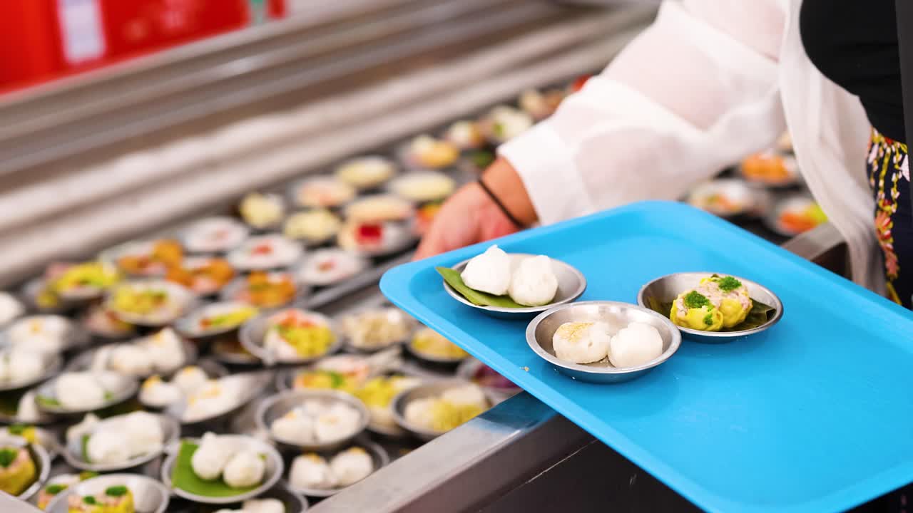 A person picks dim sum dishes from a conveyor belt in a brightly lit restaurant setting