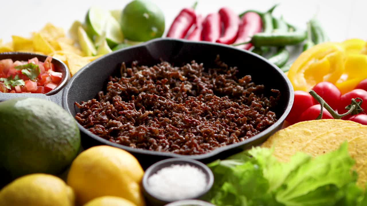 Zutaten für Chili con Carne in gusseiserner Pfanne auf weißem Holztisch