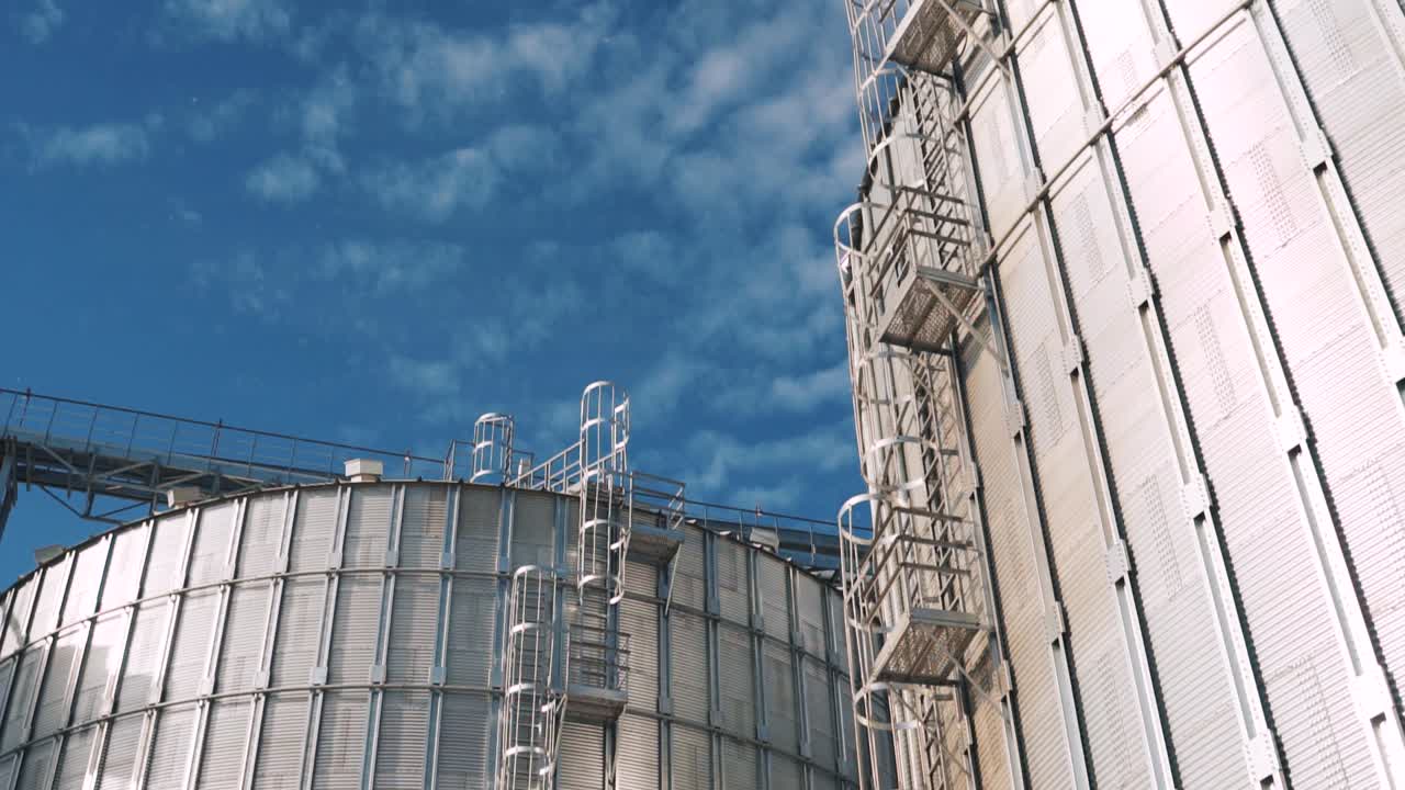 White smoke from chimneys at a grain elevator. Large silver granary. Metal industrial silos for agribusiness