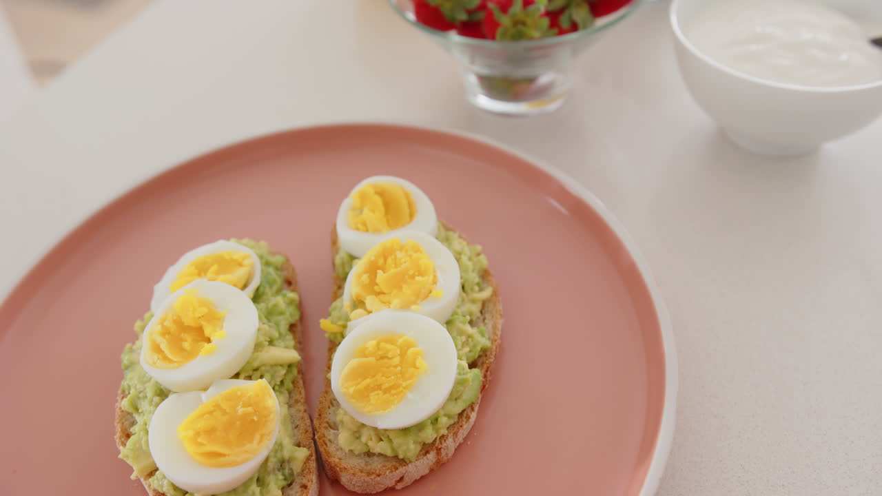 Avocado toast with boiled eggs on plate, strawberries and yogurt in background, at home