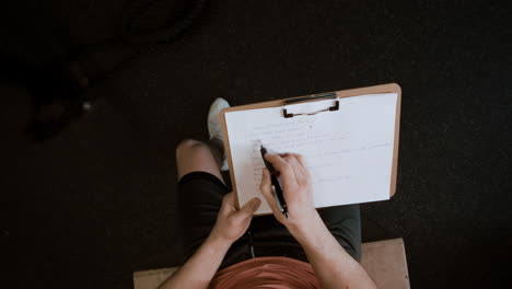 man writing down fitness workout routine in gym