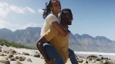 Afroamerikanischer-Mann-Gibt-Seiner-Frau-Huckepackfahrt-Am-Strand