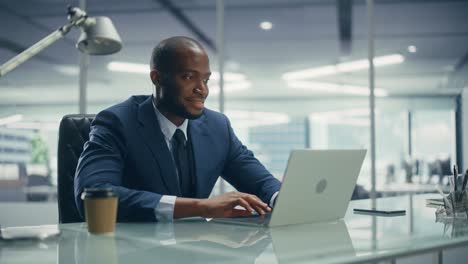 top management modern office: successful black businessman in tailored suit working on laptop computer. professional african american ceo managing investment strategy. portrait of top manager