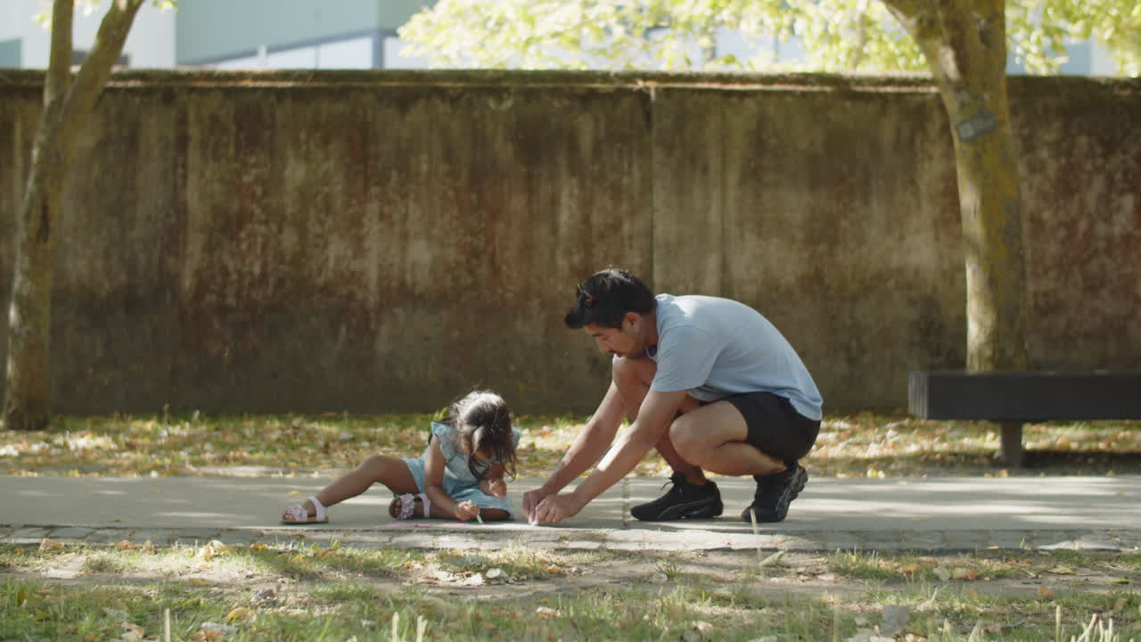 Young Asian father and daughter drawing on asphalt with chalks