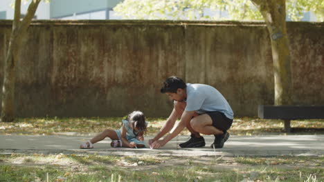 young asian father and daughter drawing on asphalt with chalks