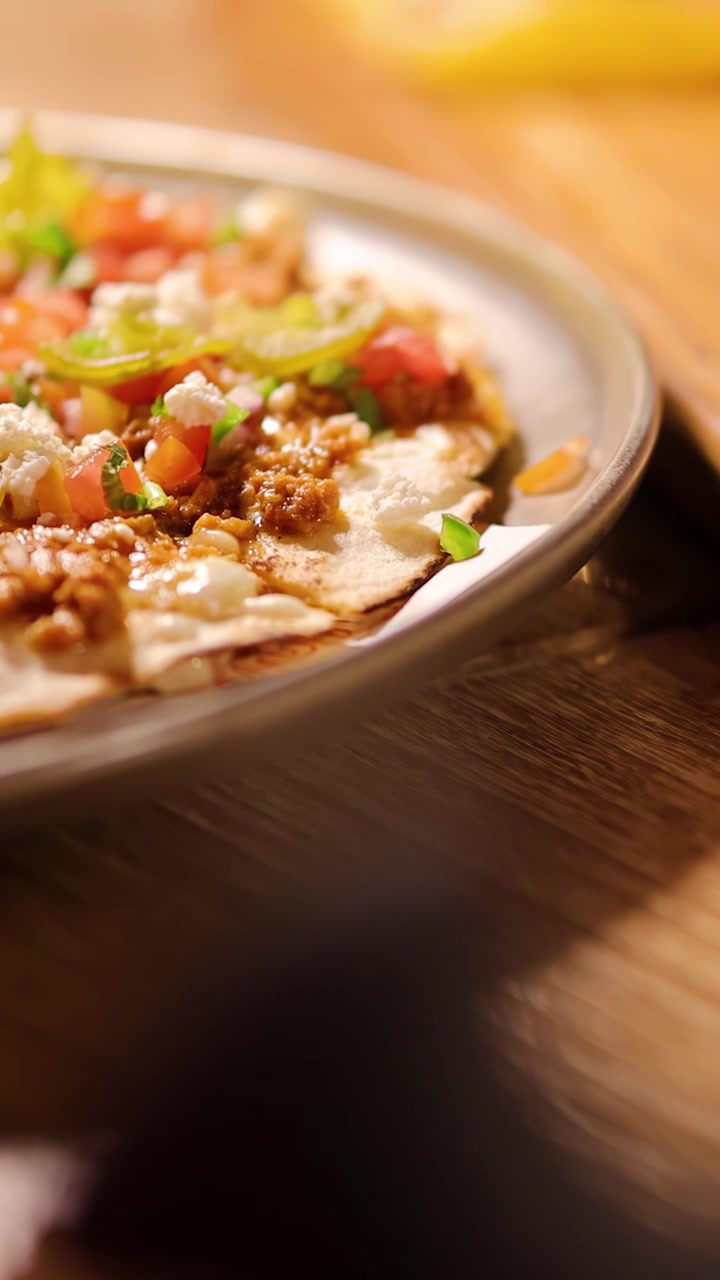 Primo piano di una mano che posiziona un taco su un tagliere di legno, illuminazione calda, profondità di campo ridotta.