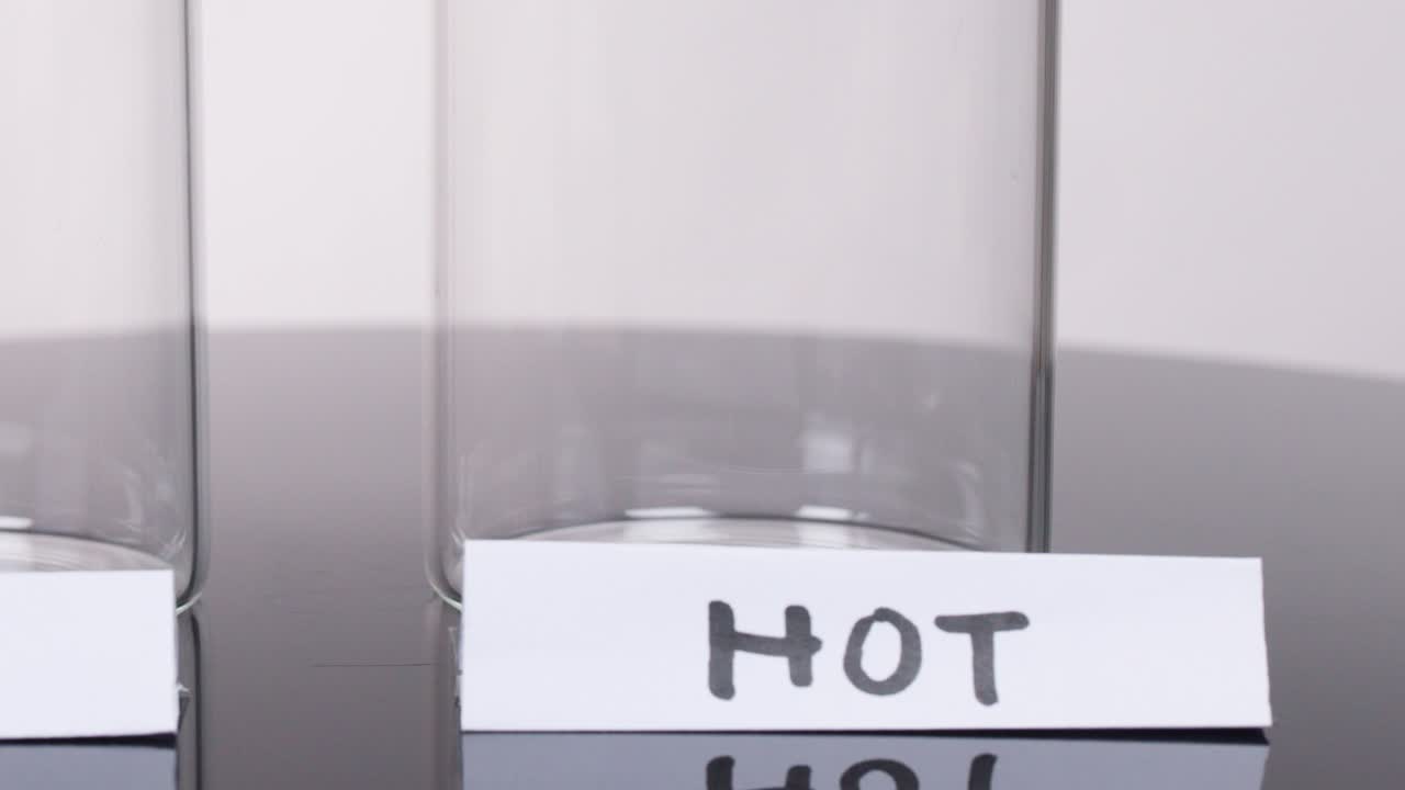 Human hand places handwritten 'HOT' label on empty glass in bright, controlled studio lighting