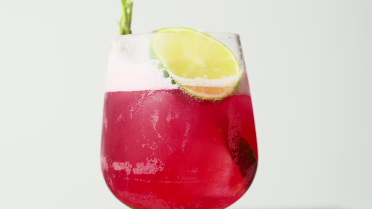 Nærbillede af en rød cocktail med is og lime på en hvid baggrund