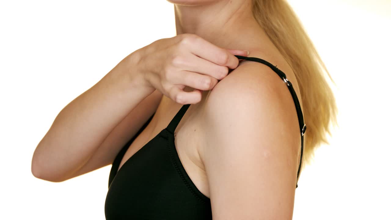 The woman in underwear corrects the shoulder strap in her bra.