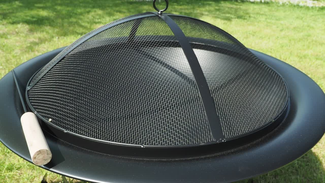 Metal bowl for fire on a background of green grass. Metal fire bowl with lid.