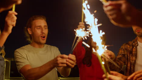 amigos multiétnicos disfrutando de una fiesta de cumpleaños en el techo. gente quemando chispas.