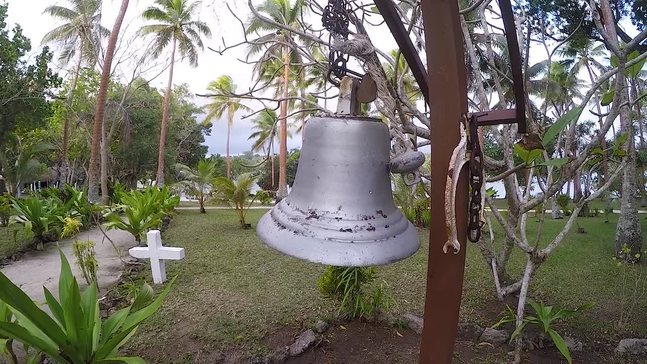 Uma mulher tocando um sino grande perto de um cemitério em uma ilha.