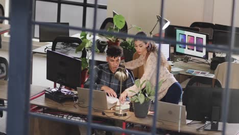 two diverse creative designers in discussion at computer in casual office, slow motion