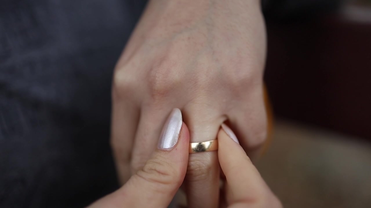 Primo piano dettagliato di una mano che toglie delicatamente una fede nuziale d'oro da un dito, catturando intimità, emozione e la transizione di una relazione sotto una luce naturale soffusa, con composizione a fuoco.