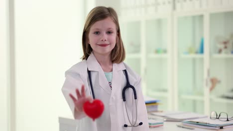 a young girl dressed as a doctor holds out a red heart