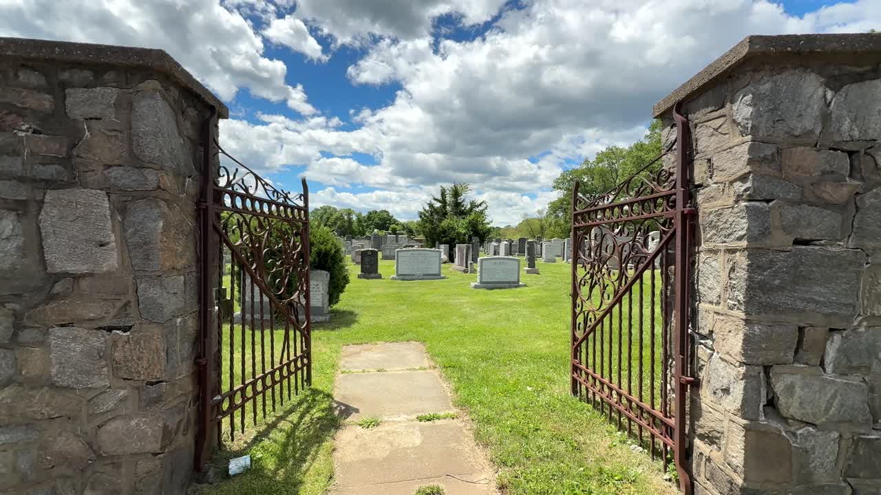 Old Jewish cemertary panning up through metal gate of many head stones laid to rest during cloudy daytime sky