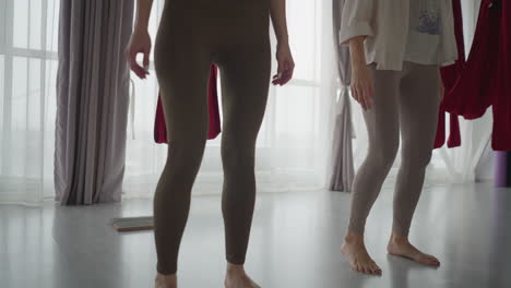 downward view of yoga enthusiasts gracefully shifting legs and bodies in soft-lit studio with sheer curtains and red hammocks, emphasizing balance, rhythm, and fluid movement in mindful practice