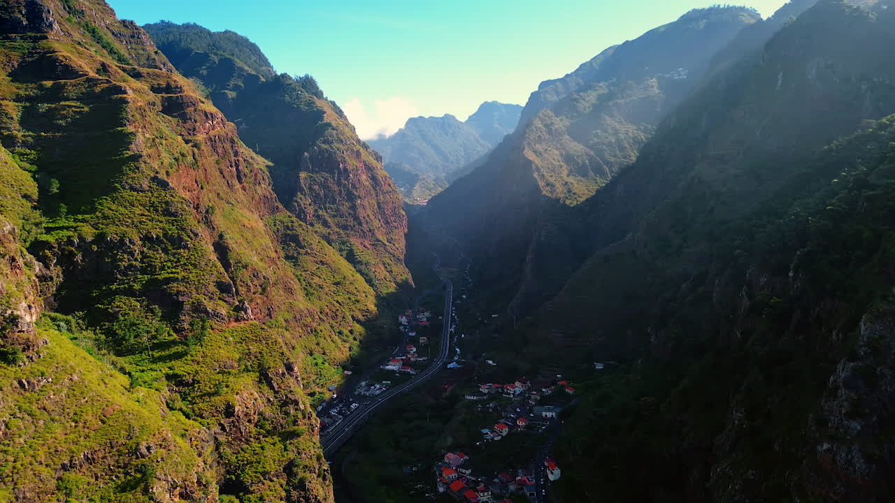 Town hiding between two high mountains with a highway crossing the scenery. Inhabited area in the rocks of the Madeira Islands, Portugal. Top view.