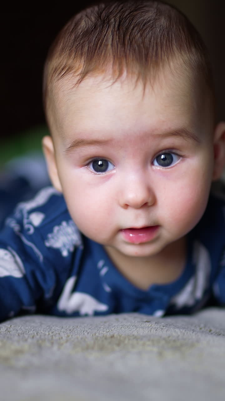 Beautiful child lies on belly keeping head steadily and looking around and down. Adorable kid close up. Vertical video