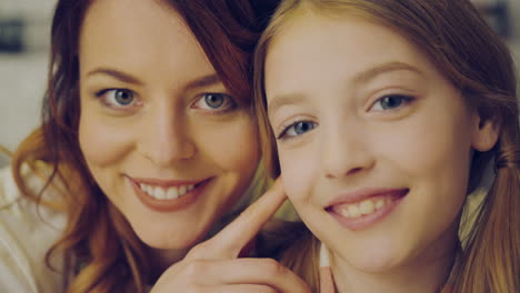 close up of the beautiful mother and her teen daughter standing closely cheek to cheek and smiling in the camera. portrait. indoor