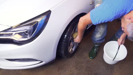 trabajador rociando agua y lavando la llanta y las ruedas, de un automóvil todoterreno blanco, en un lavadero de automóviles, en suecia