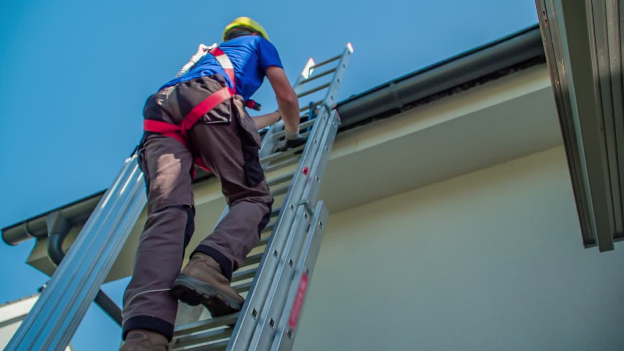 Secured professional male worker climbs up ladder on roof on sunny day