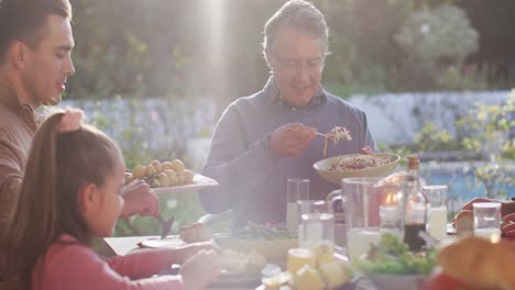 Video-Von-Glücklichen-Kaukasischen-Eltern,-Töchtern-Und-Großeltern,-Die-Essen-Am-Tisch-Im-Freien-Servieren