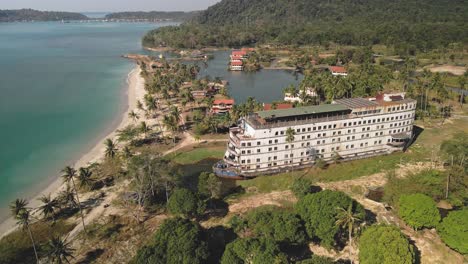 drone moving along the white sand beach with old ferry boat like structure drone passing along the coastal beach without people