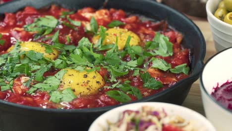 israeli cuisine. hands putting shakshuka decorated with parsley close-up. national jewish dish made of eggs fried in tomato sauce, hot peppers, onions and spices, middle eastern culture