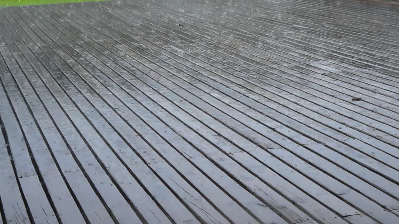 Close view of heavy rainfall hitting an old wooden deck, with visible splashes and wet textures as the camera slowly pans across the soaked surface