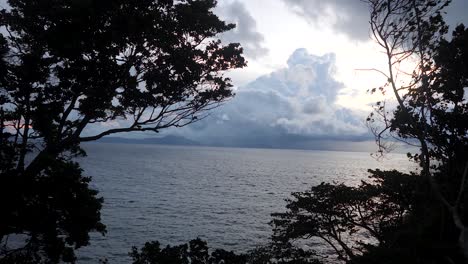 Rain-falls-along-island-coastline,-nature-silhouettes,-sunset-scenery